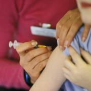 A child about to be given the MMR (mumps, measles, rubella) vaccination into their arm by a surgery nurse with a hypodermic syringe, England, UK..