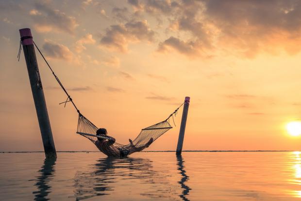 The Bolton News: A man relaxing over the water in a hammock. Credit: Canva