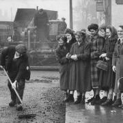 A group of mills girls, during their dinner hour, watching workmen asphalting in January, 1956